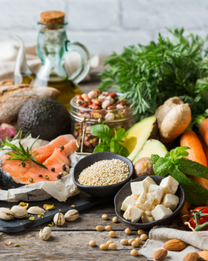 an arrangement of food items including salmon, tofu, almonds, soy beans, pistachios, turmeric, carrots, tomatoes, ginger, avocado, bread, olive oil.