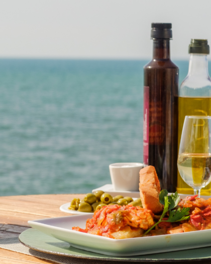 Mediterranean view with a plate of classic Mediterranean food, olive oil and wine, in reference to brain health. Robert Rose Books